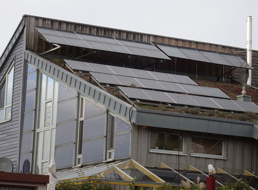 Ein Zweifamilienhaus mit Pult- und Grasdach. Dach und Fassade sind mit Photovoltaikmodulen bestückt.